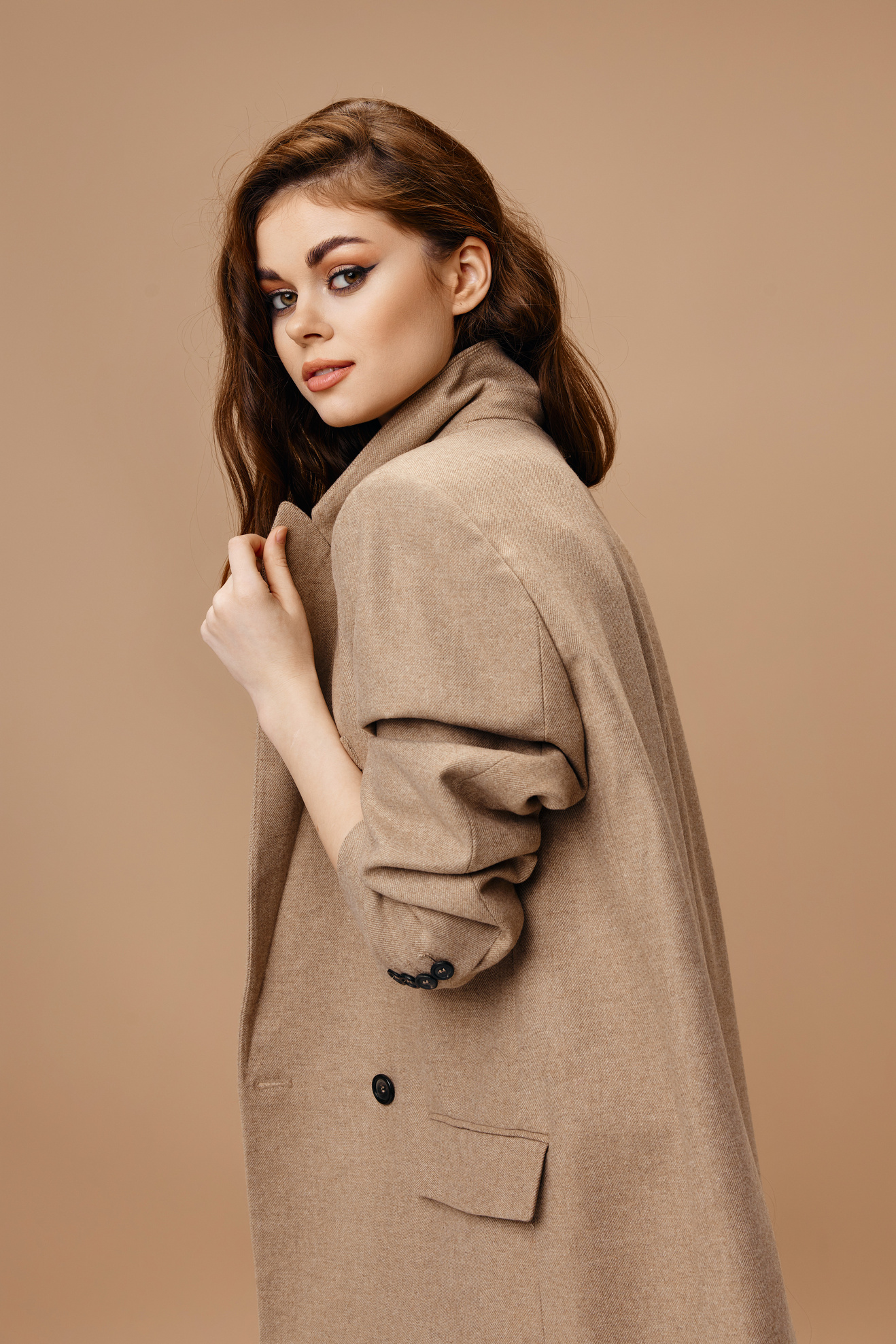 Beautiful Young Woman in a Coat on a Beige Background Straightens the Collar